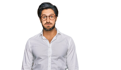 Young hispanic man wearing business shirt and glasses puffing cheeks with funny face. mouth...