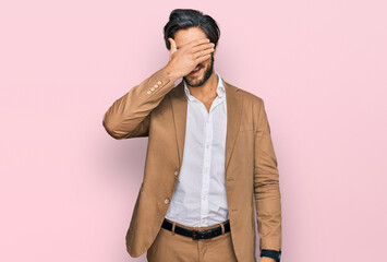 Young hispanic man wearing business clothes smiling and laughing with hand on face covering eyes for surprise. blind concept.