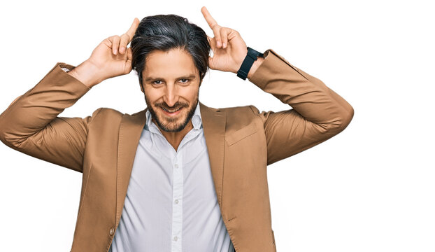 Young hispanic man wearing business clothes posing funny and crazy with fingers on head as bunny ears, smiling cheerful