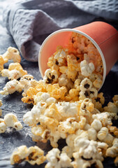 A red cup of popcorn is on the table. Sweet popcorn is on the table.