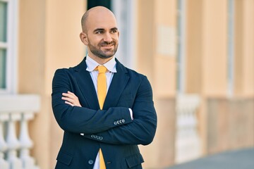 Fototapeta premium Young hispanic bald businessman with arms crossed smiling happy at the city.