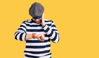 Young handsome man wearing burglar mask looking at the watch time worried, afraid of getting late