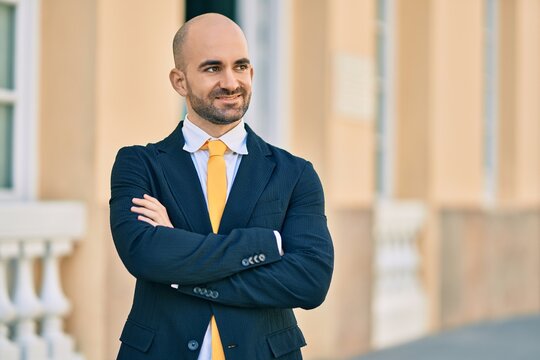 Young hispanic bald businessman with arms crossed smiling happy at the city.