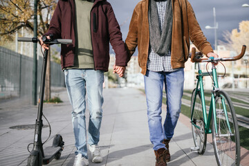 Two boys holding hands while walking with a bicycle and an electric scooter.