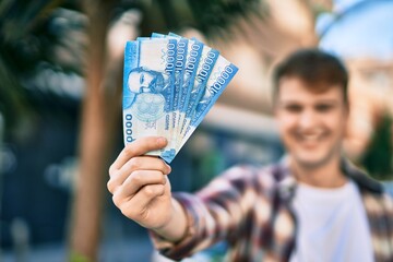 Young caucasian man smiling happy holding chile pesos banknotes at the city.