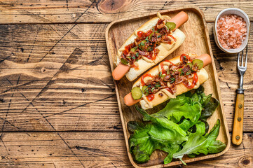 Hot dogs with fried bacon, onion and pickled cucumbers. wooden background. Top view. Copy space