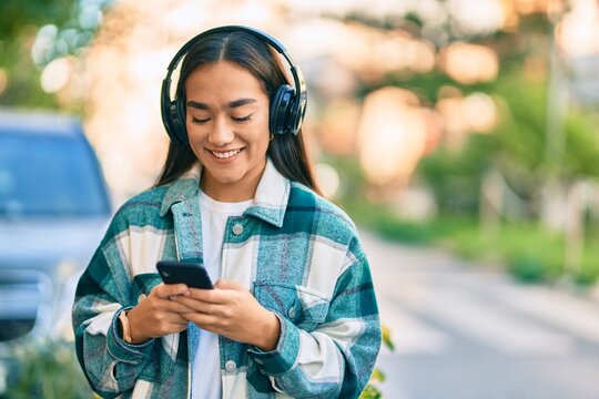 Young latin girl smiling happy using smartphone and headphones at the city.