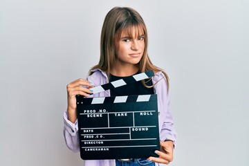 Teenager caucasian girl holding video film clapboard skeptic and nervous, frowning upset because of...
