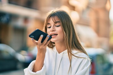 Caucasian sporty teenager girl sending voice message using smartphone at the city.
