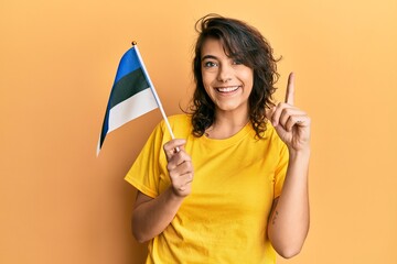 Young hispanic woman holding estonia flag smiling with an idea or question pointing finger with...