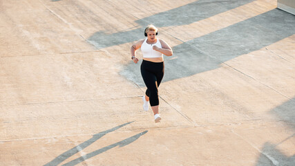 High angle view of plus size woman running outdoors. Young curvy female in sportswear jogging on roof.