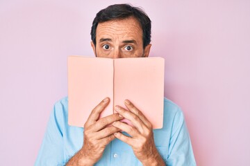 Middle age hispanic man reading book clueless and confused expression. doubt concept.