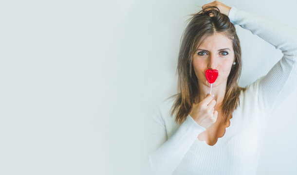 a blonde girl has a heart-shaped lollipop on her lips. Kissing a red candy lollipop. happiness and love concept.