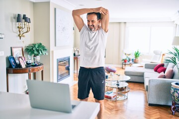 Middle age man with beard training and stretching doing exercise at home looking at sport video on computer