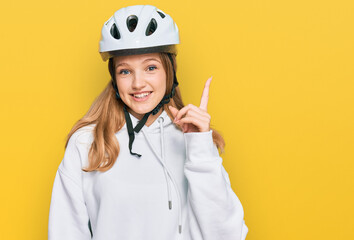 Beautiful young caucasian girl wearing bike helmet pointing finger up with successful idea. exited and happy. number one.