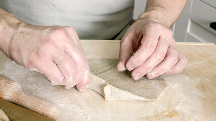 A man without a face bakes national rye dough pies with potato filling. Hands and dough close-up....