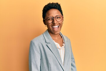 Young african american girl wearing business jacket and glasses winking looking at the camera with...