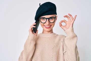 Young caucasian woman wearing french style having conversation talking on the smartphone doing ok sign with fingers, smiling friendly gesturing excellent symbol
