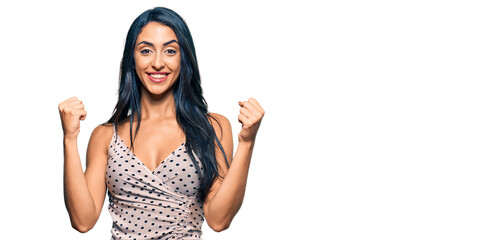 Obraz premium Beautiful hispanic woman wearing summer dress screaming proud, celebrating victory and success very excited with raised arms