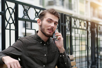 Young man sits on bench and talks on smartphone