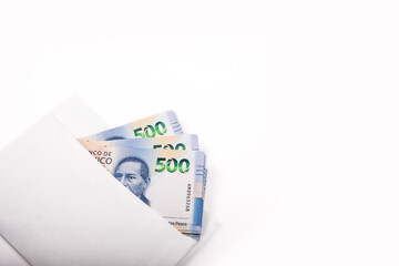 Billetes mexicanos dentro de un sobre blanco, sobre fondo blanco esquinado.
Mexican peso bills inside a white envelope, on a white background.