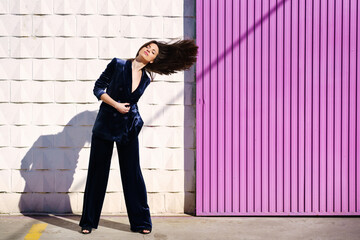 Woman wearing blue suit posing near pink shutter, moving her hair.