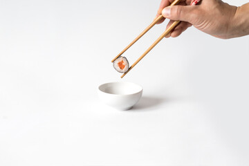 Man's hand picking up sushi with chopsticks and dipping in soy sauce.