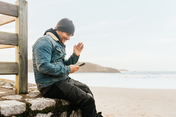 young man sitting making a video call with his smartphone on the beach. communications.