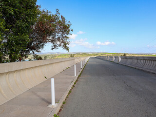 Straight road leading along the top of the dam. Lots of wind turbines in the background.