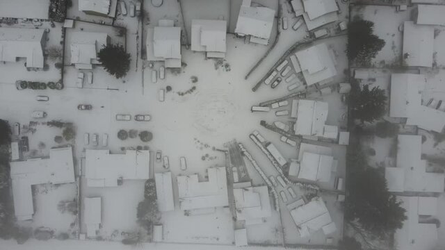 Aerial View Of Neighborhood Cul De Sac With Snow Covered Houses In A Winter Storm. A Truck Is Towing A Person On A Sled Behind It In The Ice. 