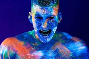 Young man shouts. Fluorescent paint on face and muscular torso, in studio shot with UV light