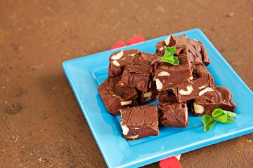Sliced homemade fudge chocolates made from dark chocolate, condensed milk and hazelnuts on a blue plate on a brown concrete background. Candy recipes. American cuisine.