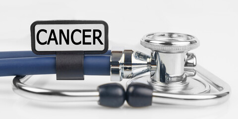 On the white surface lies a stethoscope with a plate with the inscription - CANCER