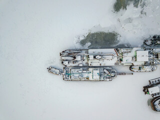 Aerial drone view. Cargo ships in a frozen bay. Cloudy frosty winter day.