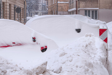 There are cars on the streets of the city. They are covered with a lot of snow. Winter disaster.