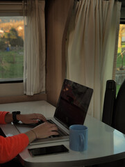 Hands of a woman with a laptop, phone and coffee in a camper van