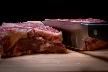 A Knife Cutting through a Raw Piece of Ribeye Steak on a Cutting Board with a Black Background