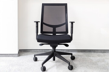 Modern black office chair in an empty office against white wall on gray carpet