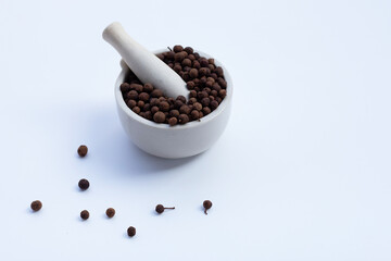 Allspice in porcelain mortar with pestle on white