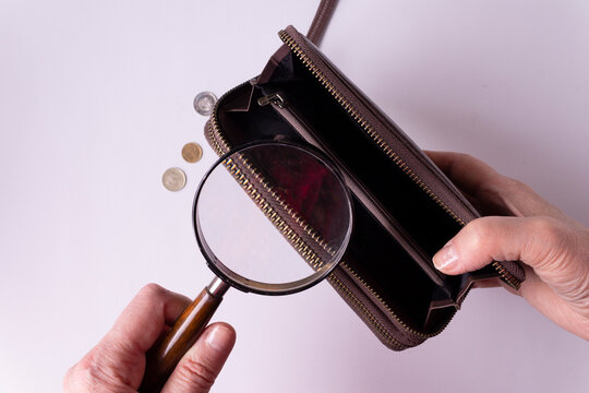 A Man's Hand Holds A Magnifying Glass Over An Open Empty Wallet On A White Background. Horizontal Orientation. View From Above.