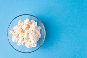 Cottage cheese in a glass plate on a blue background. Horizontal orientation. View from above.