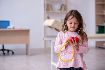 Small girl holding stethoscope waiting for doctor in the clinic