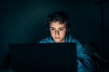 Young blogger and video game streamer playing at home with laptop. Vlogger filming himself having fun using technology to connect with audiences.Teenager play with online friends using gaming console.