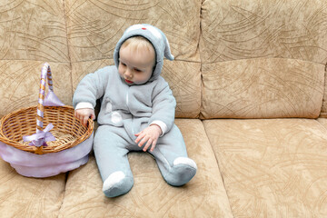 Naklejka premium Cute little toddler baby boy wearing a bunny, rabbit costume with basket sitting on couch. easter card