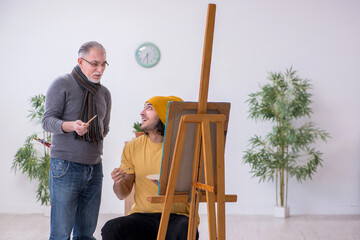 Young man taking lesson from old painter