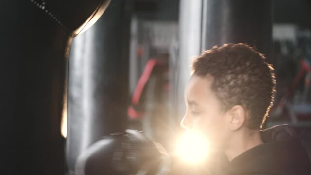 A school-aged boy is boxing at dark gym. African american.