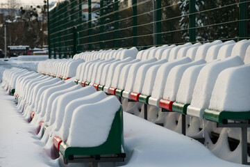 Raws of outdoor stadium seats heavily covered with snow "caps" in winter. Selective focus.