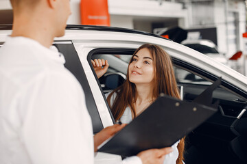 Lady in a car salon. Woman buying the car. Elegant woman in a white blouse. Manager with a client