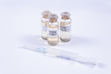 on a white background there is a syringe behind it there are three vials of covid-19 vaccine