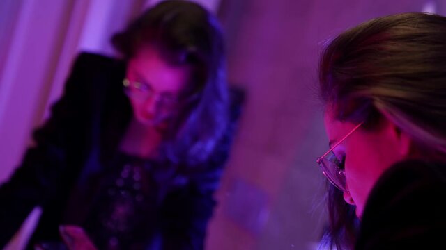 A brunette woman with round glasses is in the bathroom, standing in front of the mirror, rinsing her mouth and spitting water.